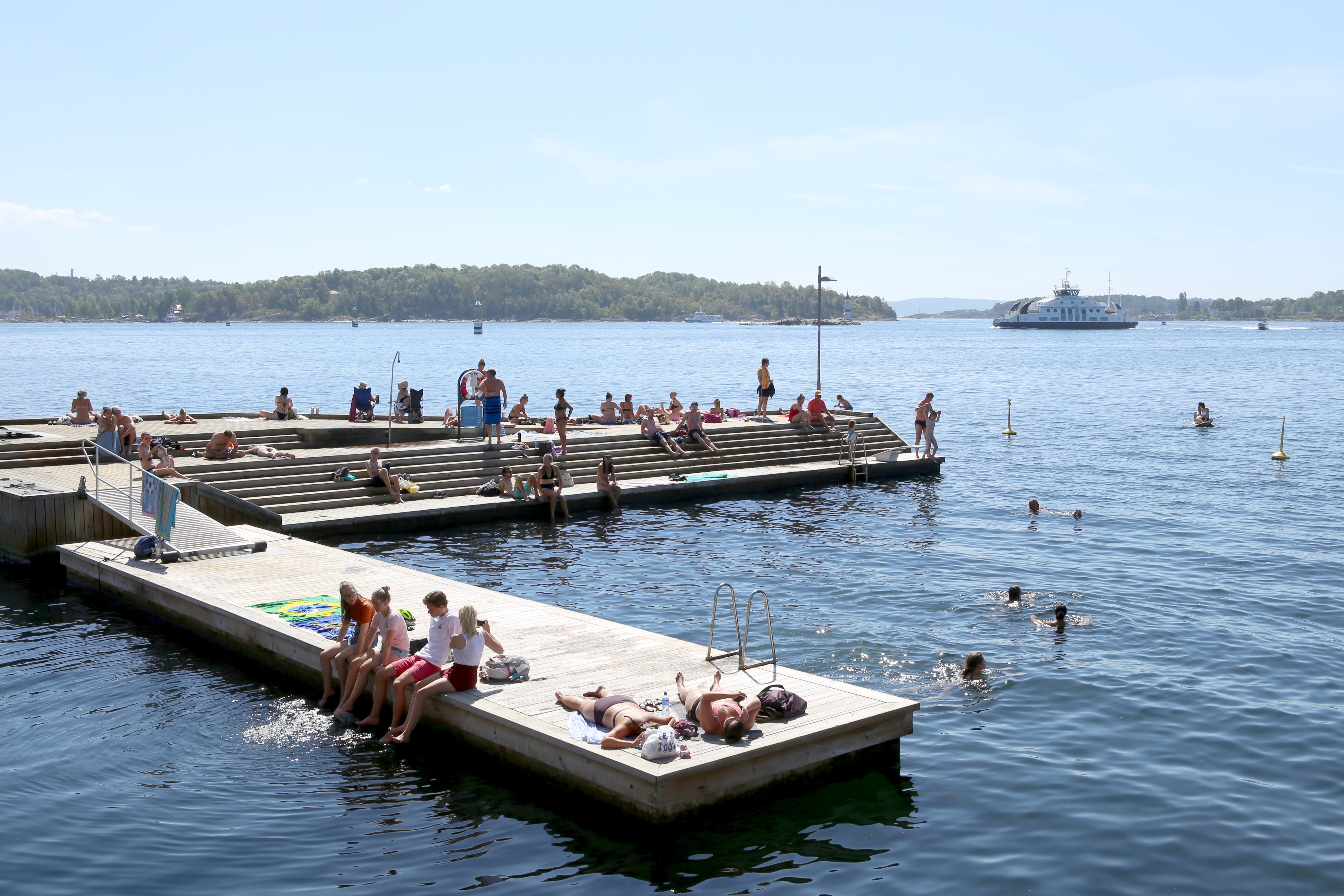 En brygge med folk som soler seg og folk i vannet som bader.